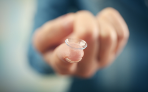  Image shows a contact lens balanced on the index finger of an extended hand.
